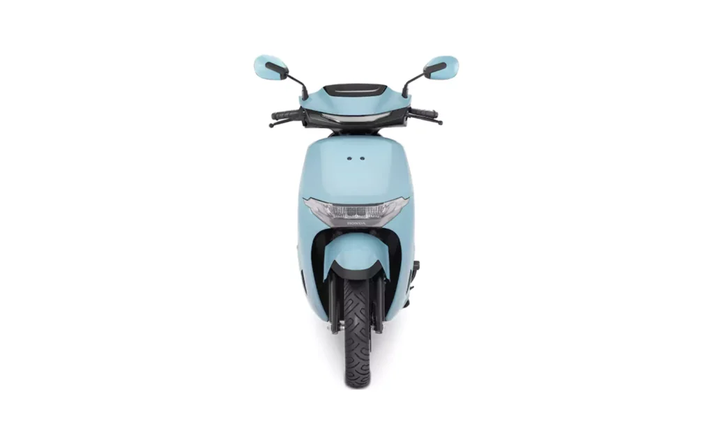Front view of a light blue Honda Activa e electric scooter, showing its headlamp, handlebars, and front wheel, set against a plain white background