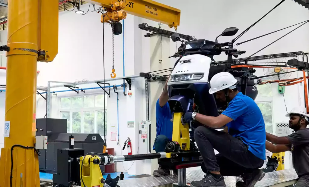 Engineers assembling Ather Rizta electric scooter in factory wearing safety gear and helmets.